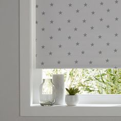 two vases sit on a window sill in front of a gray and white star patterned roman blind