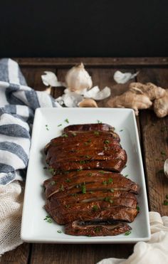 sliced up meat on a white plate with garlic and parsley next to it, sitting on a wooden table