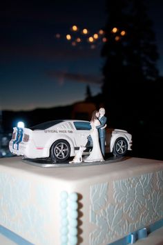 a wedding cake with a white car on top and blue ribbon around the edge, in front of a night sky