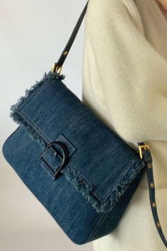 a woman wearing a white sweater and jeans holding a blue denim handbag with the letter g on it