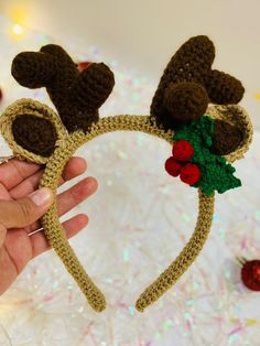 a hand holding up a crocheted reindeer headband with holly berries on it