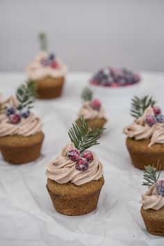 small cupcakes with frosting and berries on top sit on a white tablecloth