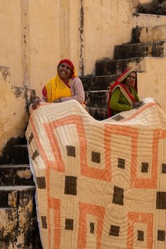 two women sitting on the steps with a large quilt