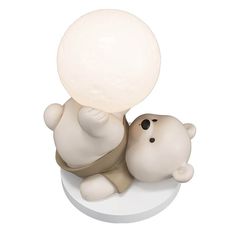 a small white teddy bear sitting on top of a table next to a light bulb