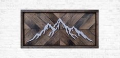 a wooden wall hanging with mountains cut out of it's sides on a brick wall