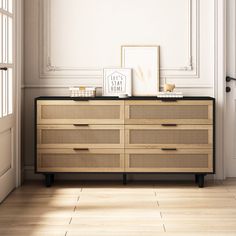 an empty room with a dresser and pictures on the top, next to a door