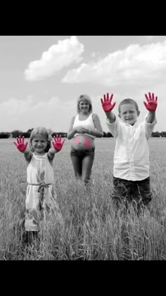 three children are standing in the grass with their hands up and one child is wearing red gloves