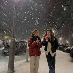 two people standing on a snowy sidewalk at night