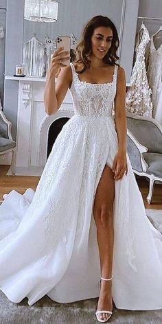 a woman taking a selfie while wearing a wedding dress with thigh high slits