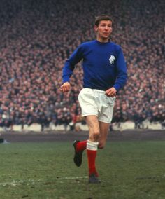 a man in blue shirt and white shorts running on soccer field with crowd behind him