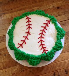 a cake decorated with green and red icing on top of a wooden table in the shape of a baseball