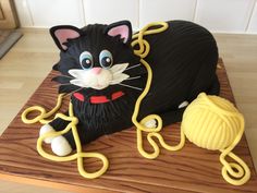 a cake with a black cat and yellow yarn on the top is sitting on a wooden board