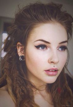 a young woman with long hair and piercings on her ears looking at the camera