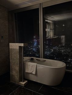 a bath tub sitting next to a large window in a bathroom with a view of the city at night