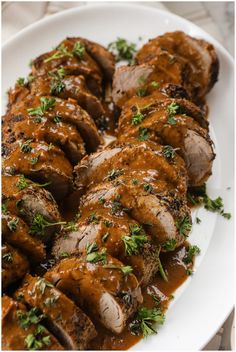 sliced meat covered in gravy and garnished with parsley on a white plate