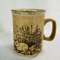 a coffee mug with an image of a rabbit in the grass on it's side