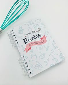 a recipe book with a whisk on top of it next to a spiral notebook