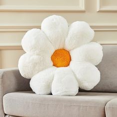 a white flower pillow sitting on top of a gray couch in front of a beige wall