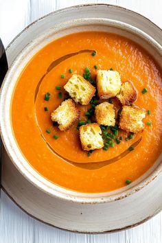 a bowl of soup with croutons and garnishes on top, ready to be eaten