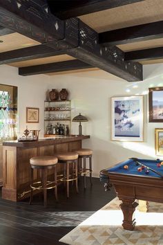 a pool table in a living room next to a bar with stools and pictures on the wall