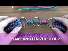 two hands are working on a colorful bracelet with metal rings and looped ends, while another hand is holding the clasp