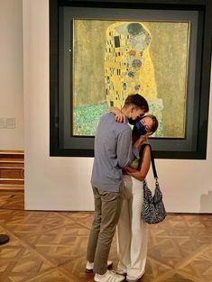 a man and woman kissing in front of a painting on display at an art museum