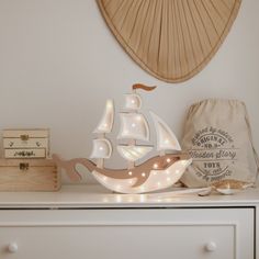 a white lamp with a sailboat on it sitting on top of a dresser next to a bag