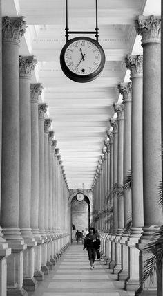 a black and white photo of people walking down a long hallway with columns on both sides