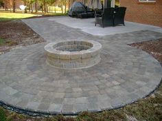 a brick fire pit sitting in the middle of a yard next to a patio area