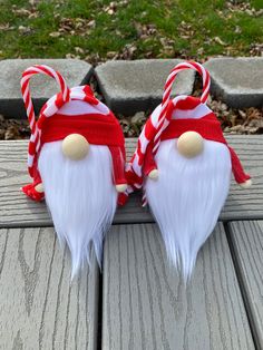 two white and red christmas gnomes with candy canes on their heads sitting on a wooden bench