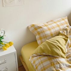 a bed with yellow and white sheets on top of it next to a night stand