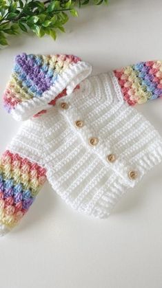 a crocheted sweater and jacket sitting on top of a white table next to green leaves