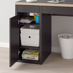 an office desk with two white baskets under it and a trash can next to it