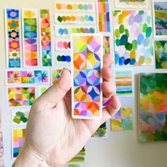 a person holding up a card in front of colorful art