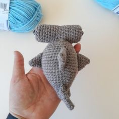 a hand is holding a small crocheted gray stuffed animal in front of two skeins of yarn