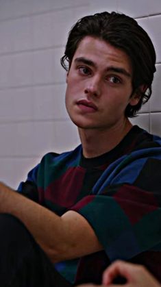 a young man sitting in front of a white brick wall