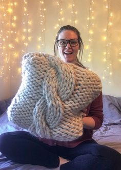 a woman sitting on a bed holding up a large knitted blanket in front of her face