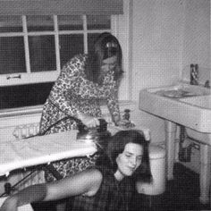 two women sitting at a sink in a bathroom with the woman standing next to her