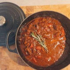 a pot filled with stew sitting on top of a wooden table next to a skillet