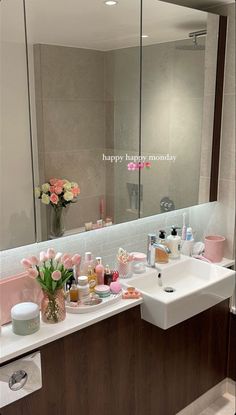 a bathroom sink sitting under a large mirror next to a counter with lots of personal care items on it