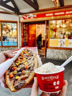 a person holding up a hot dog with toppings and ice cream in front of a store