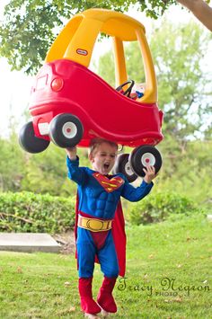 a young boy dressed as superman carrying a toy car