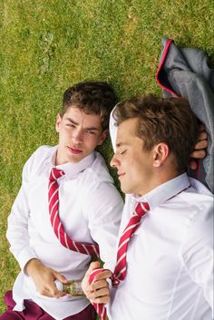 two young men laying on the grass wearing ties and looking at each other's eyes