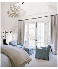 a bedroom with white walls and blue chairs in front of the bed, chandelier