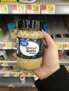 a hand holding a jar of minced garlic in front of a grocery store shelf