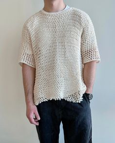 a man standing in front of a white wall wearing a knitted shirt and black pants