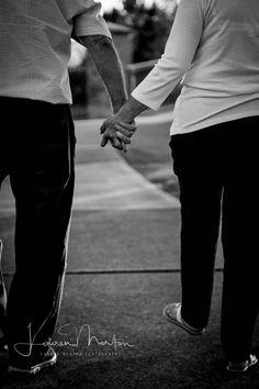 an older couple holding hands while walking down the street in black and white photo with trees in background