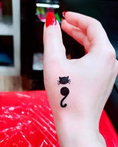 a woman's hand with a black cat tattoo on her left wrist and red nail polish