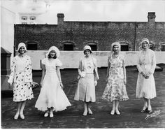 an old black and white photo of four women in dresses standing on the roof of a building