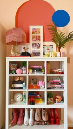 a white shelf filled with lots of books and shoes next to a potted plant